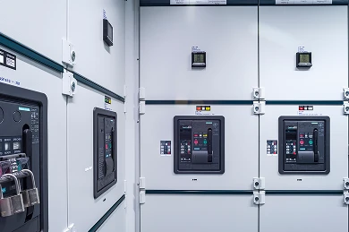 Mehrere graue Schalttafeln mit Displays in einer Elektro- bzw. Technikhalle; Blick auf Schränke von der Seite.