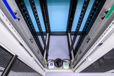 Offene Serverracks an beiden Seiten, Blick durch einen zentralen Gang mit Kabeltrassen und Kabelbündeln.