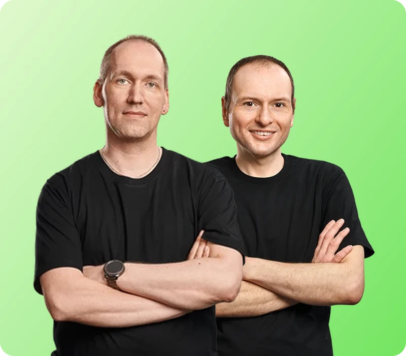 Zwei Männer in schwarzen T-Shirts stehen nebeneinander, Arme verschränkt, vor grünem Farbverlauf.