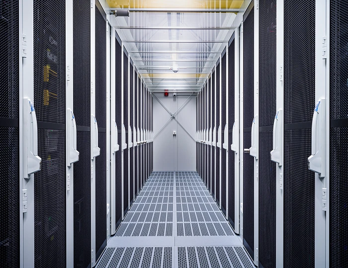 Serverracks auf beiden Seiten eines Gangs; Metallgitterboden, Decke mit Beleuchtung, Tür am Ende.